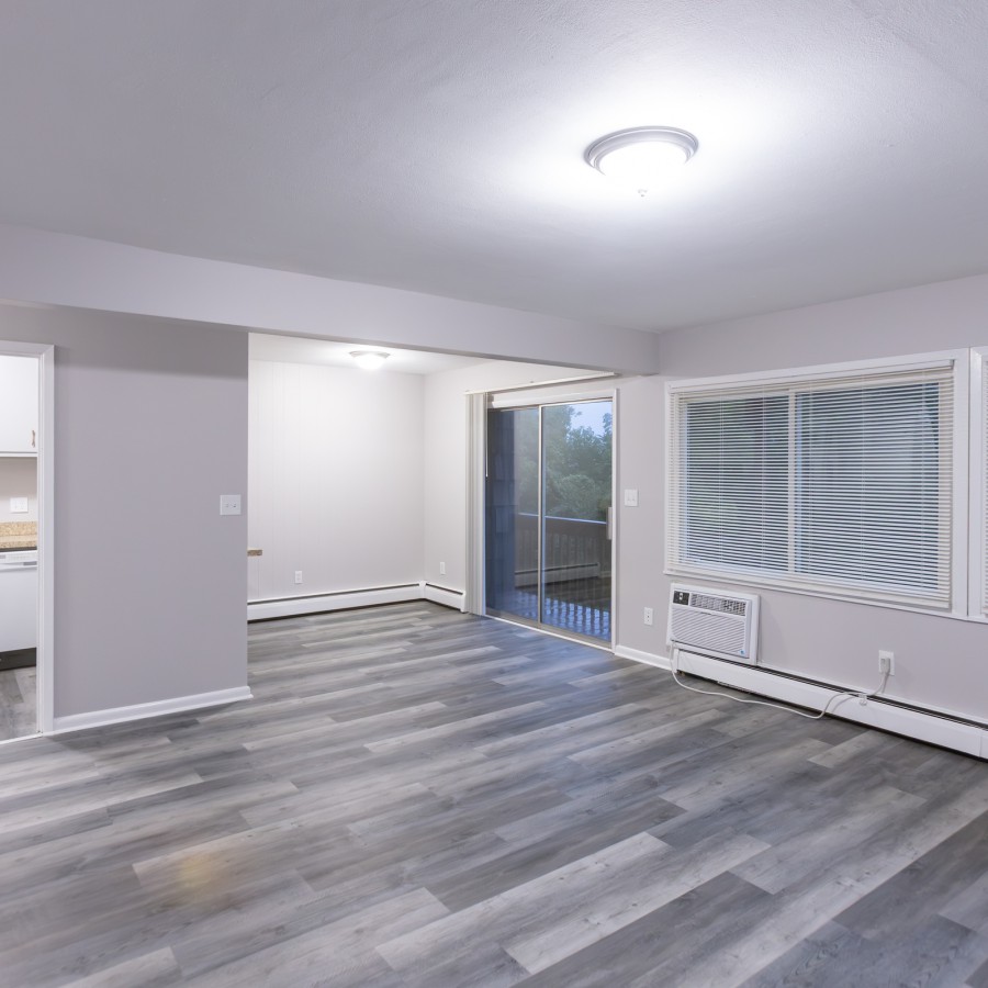 One-bedroom living room with windows and a balcony door at Carriage House Apartments, Syracuse NY