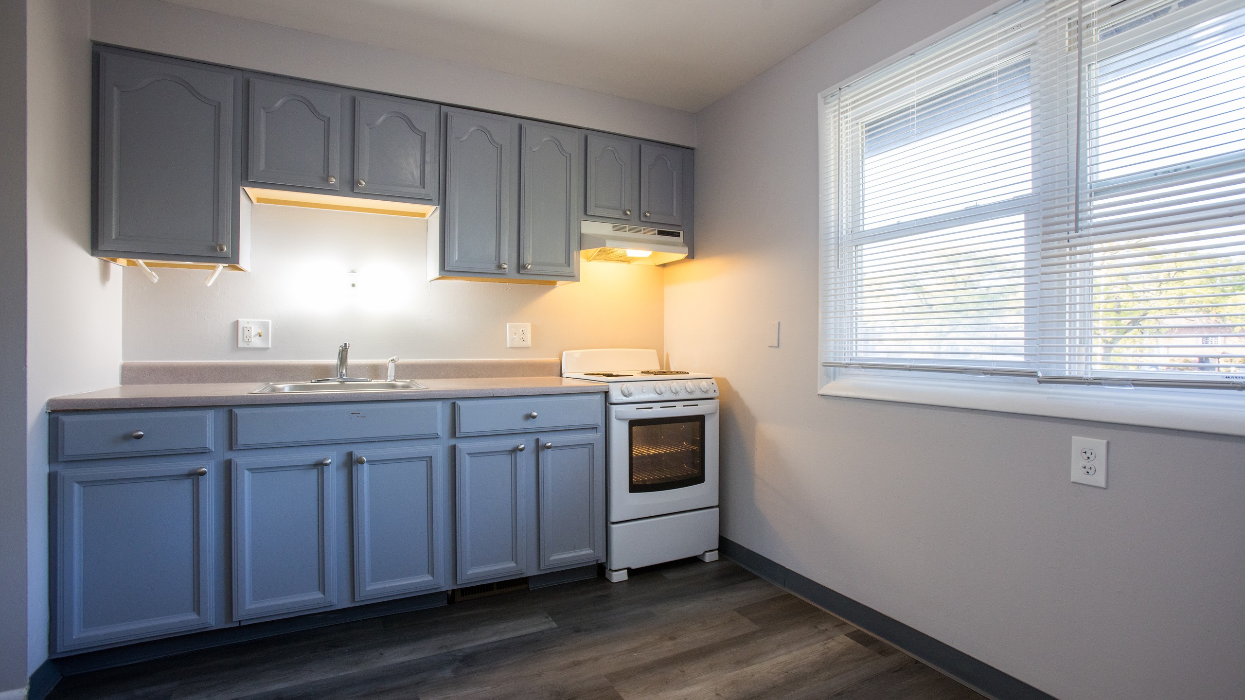 Two-bedroom kitchen with blue cabinets and window at Carriage House Apartments, Syracuse NY