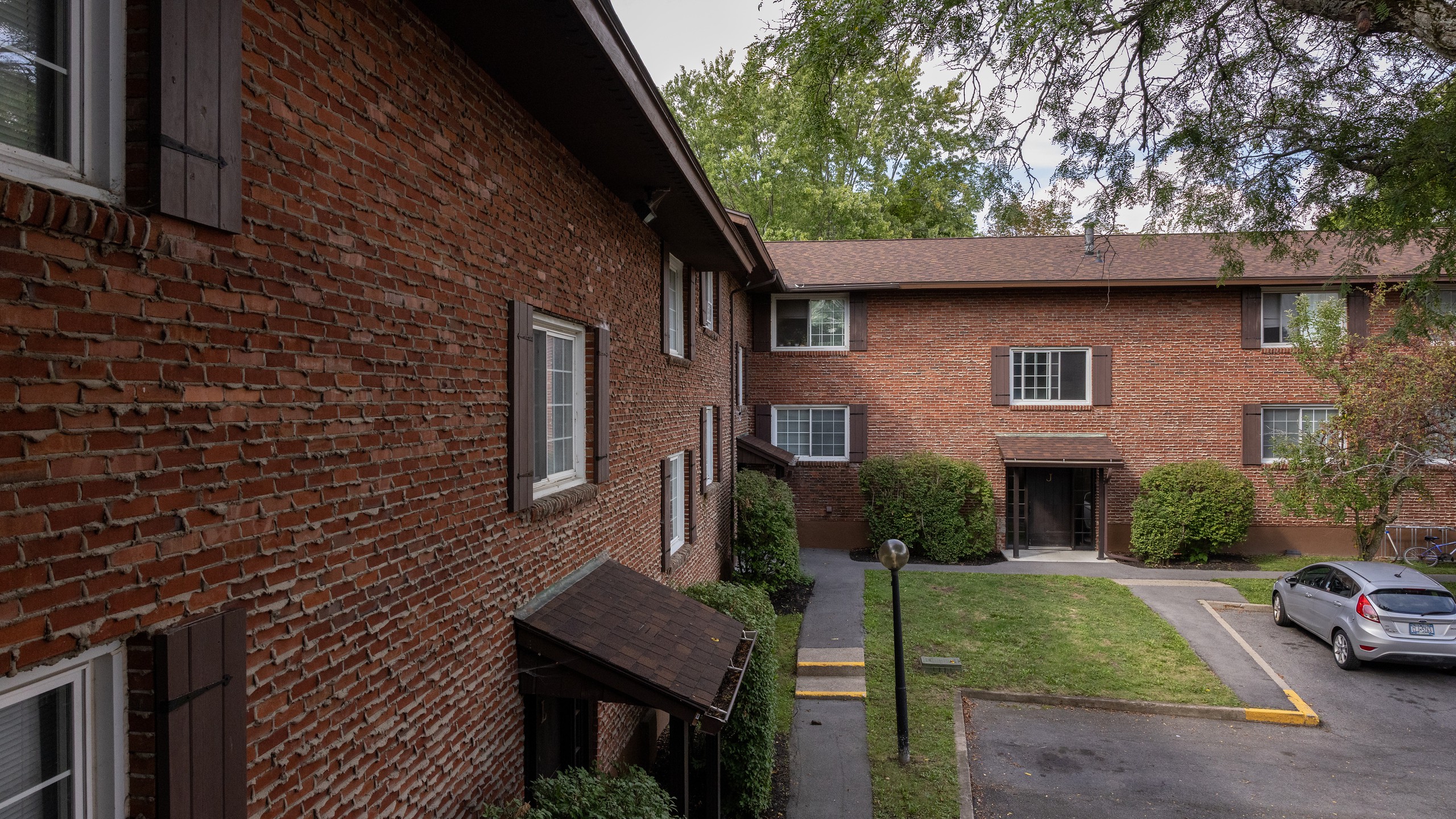 Two-story brick apartment buildings around a lawn and walkway at Carriage House Apartments, Syracuse NY