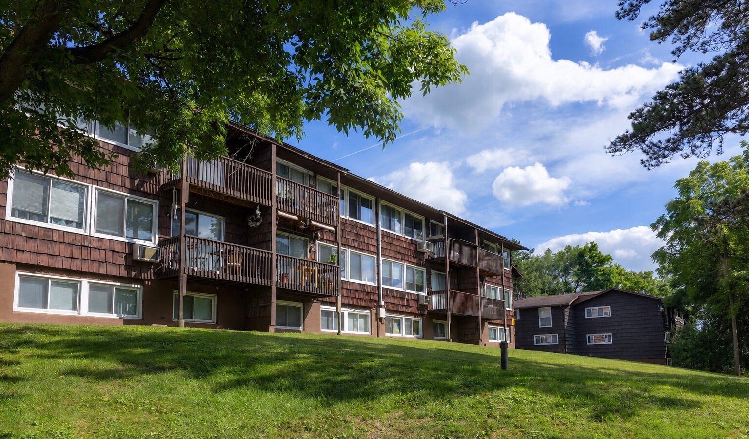 Sunny lawn below three-story buildings with balconies at Carriage House Apartments, Syracuse NY